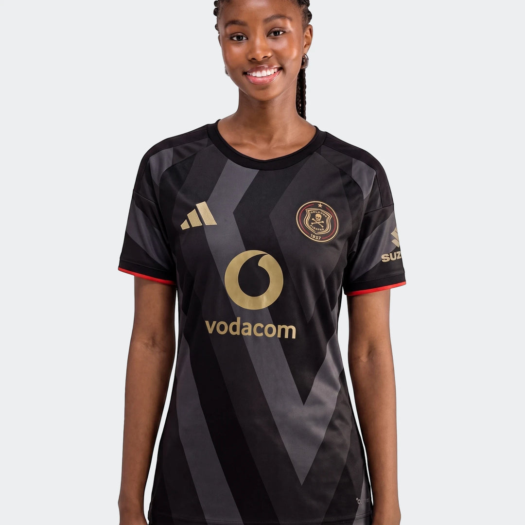 Young woman wearing an Orlando Pirates 26/27 Home Jersey, black and grey, short-sleeved, featuring gold logos.