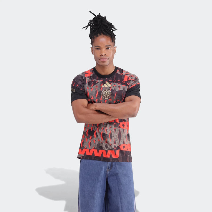 Orlando Pirates 26/27 Pre Match Jersey, a black, red, and gold patterned short-sleeve top, displayed on a male model.
