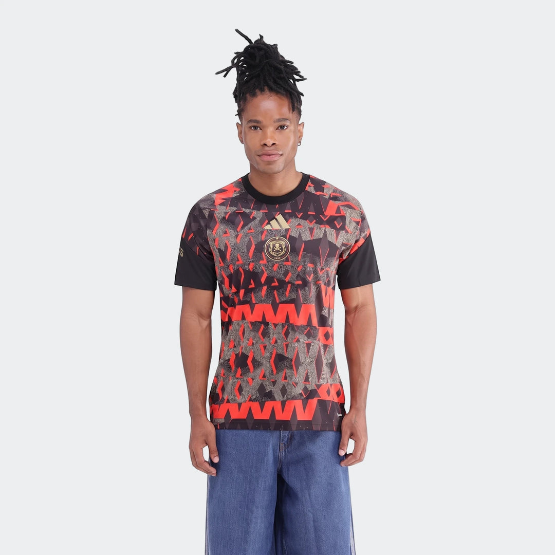 Male model wearing a black and red patterned Orlando Pirates 26/27 Pre Match Jersey and blue jeans.