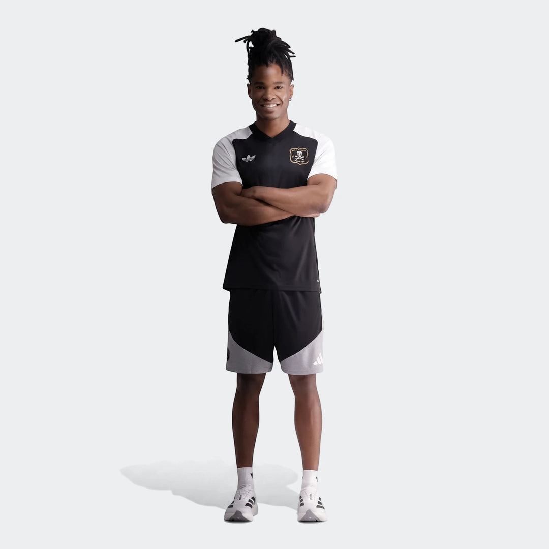 Male model wearing an Orlando Pirates 26 Pre Match Trefoil Jersey and black shorts, standing full body.