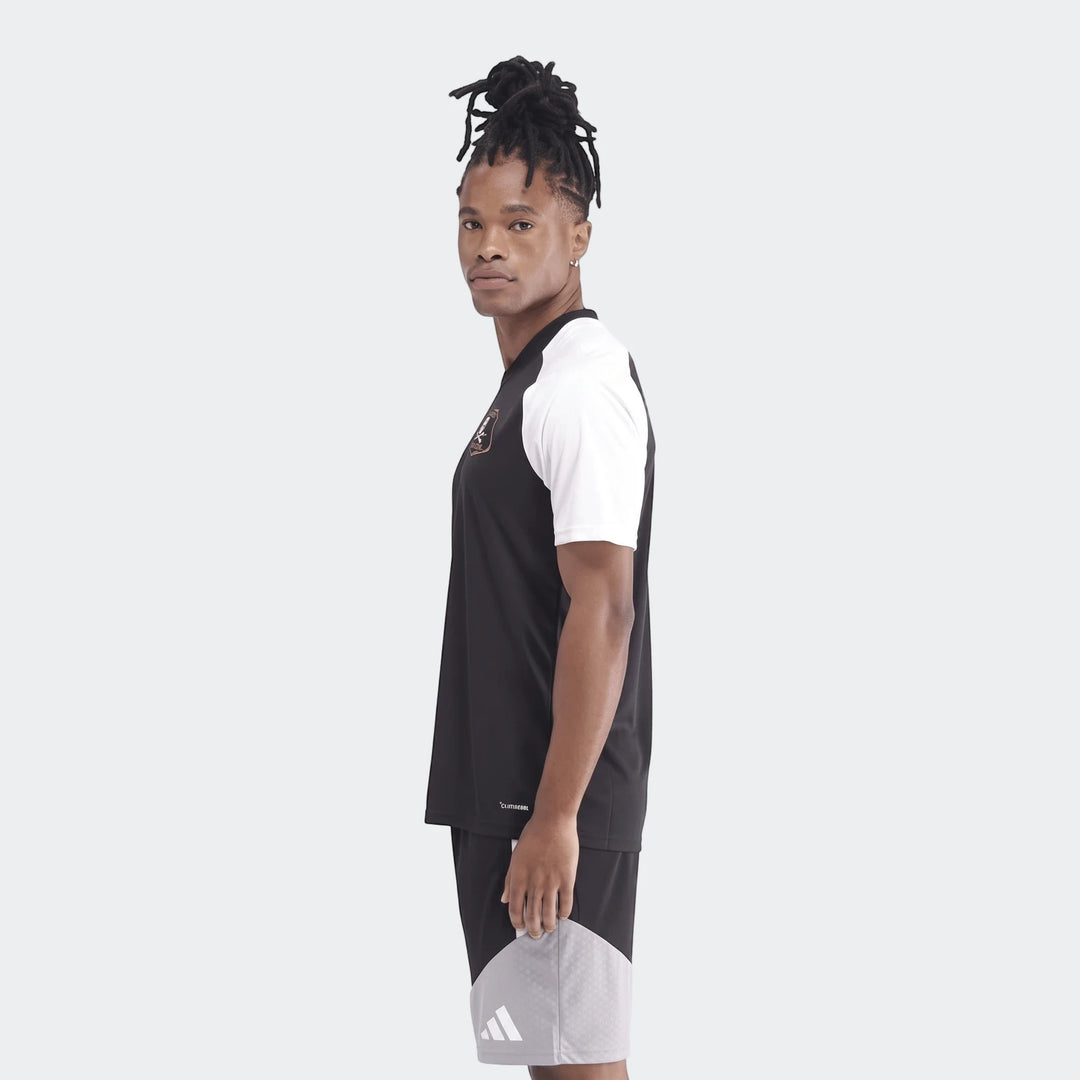 Man wearing a black and white Orlando Pirates 26 Pre Match Trefoil Jersey and black shorts, standing in side profile.