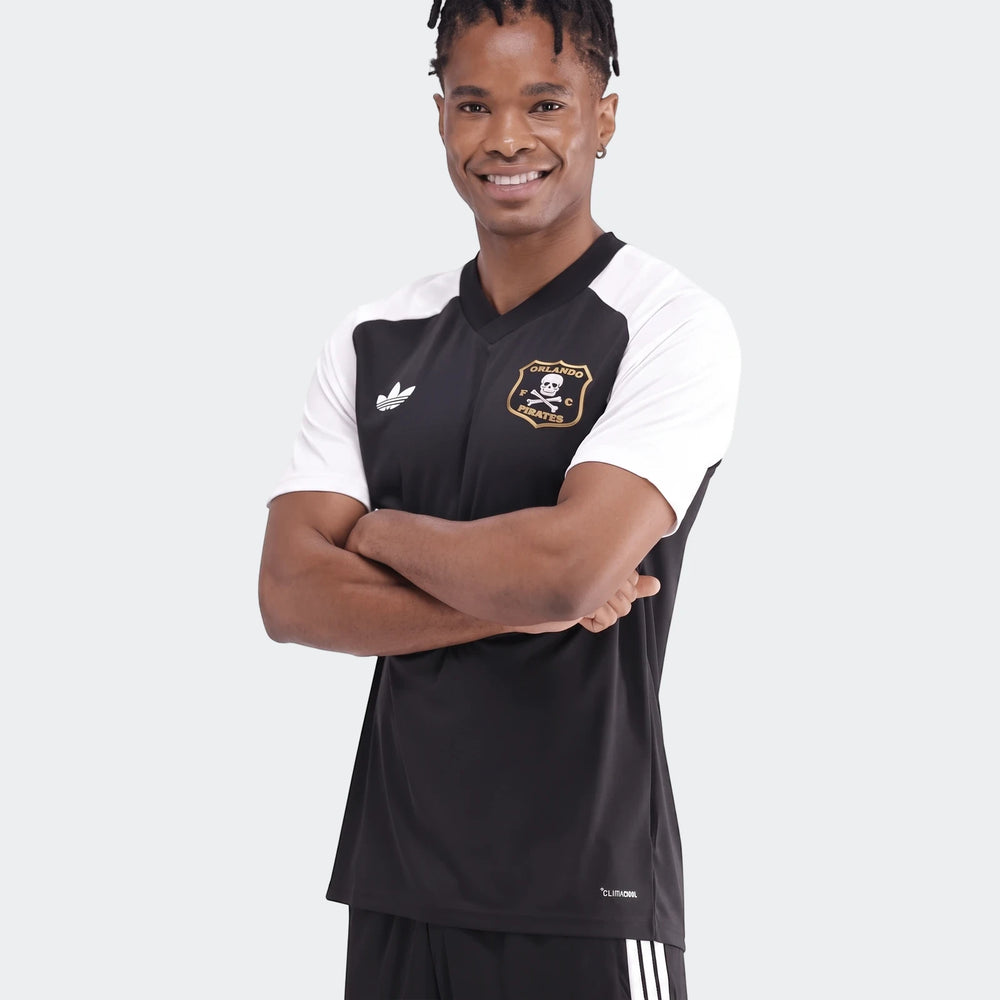 Young man wearing an Orlando Pirates 26 Pre Match Trefoil Jersey in black and white with crossed arms.