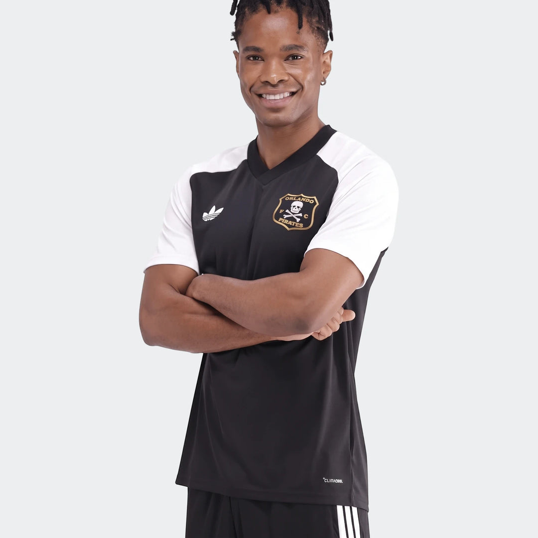 Young man wearing an Orlando Pirates 26 Pre Match Trefoil Jersey in black and white with crossed arms.