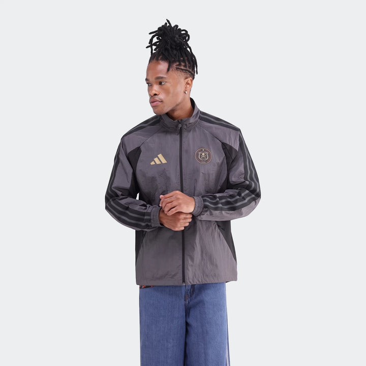 Male model wearing a gray and black Adidas Orlando Pirates Home Anthem full-zip jacket with gold logos.