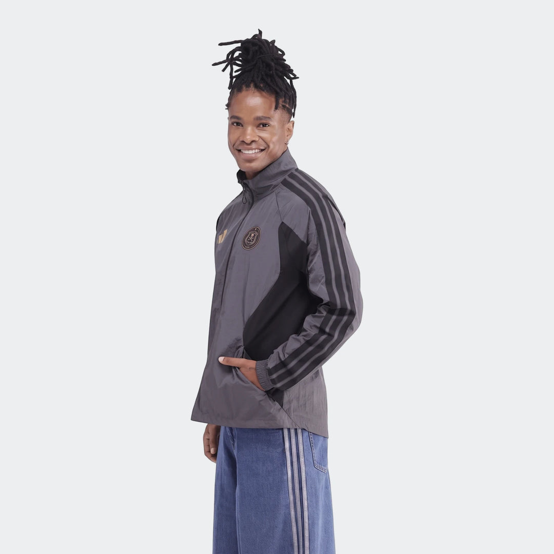 Orlando Pirates Home Anthem Jacket in gray and black, with three stripes, worn by a smiling person with dreadlocks posing