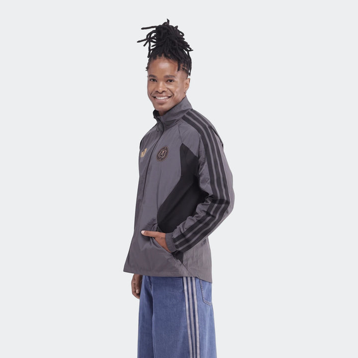 Orlando Pirates Home Anthem Jacket in gray and black, with three stripes, worn by a smiling person with dreadlocks posing
