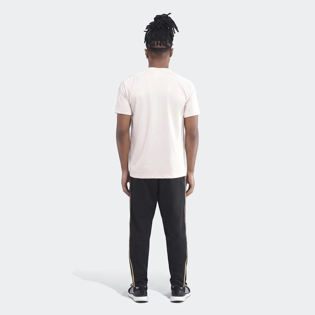 Man wearing a beige Orlando Pirates Originals T-Shirt and black track pants, shown from the back.