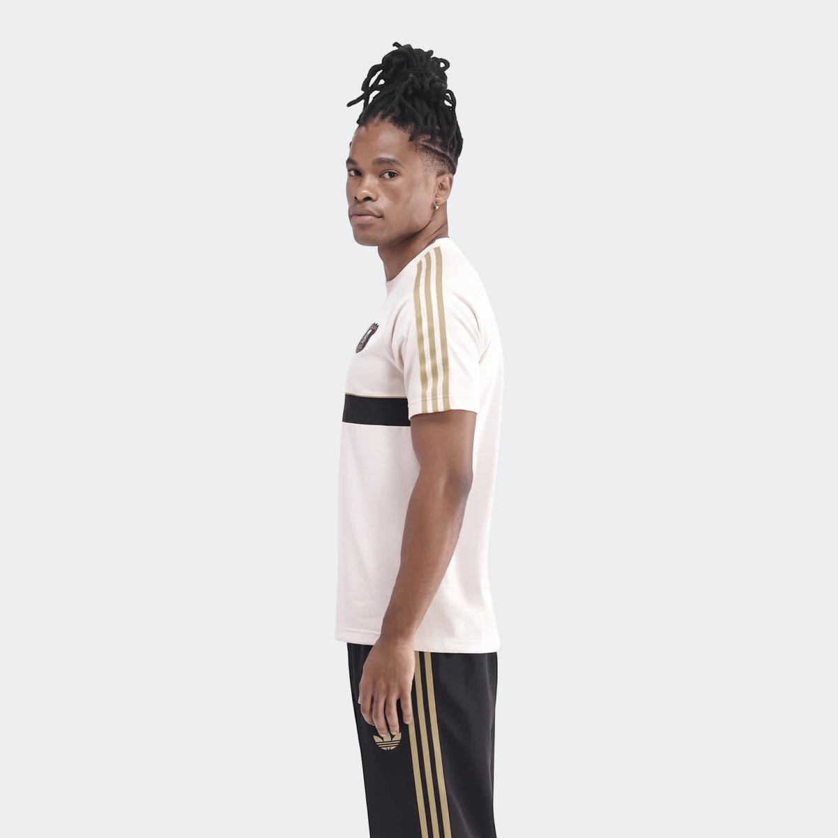Men's Orlando Pirates Originals T-shirt in cream with black and gold stripes, paired with black track pants, worn by a model