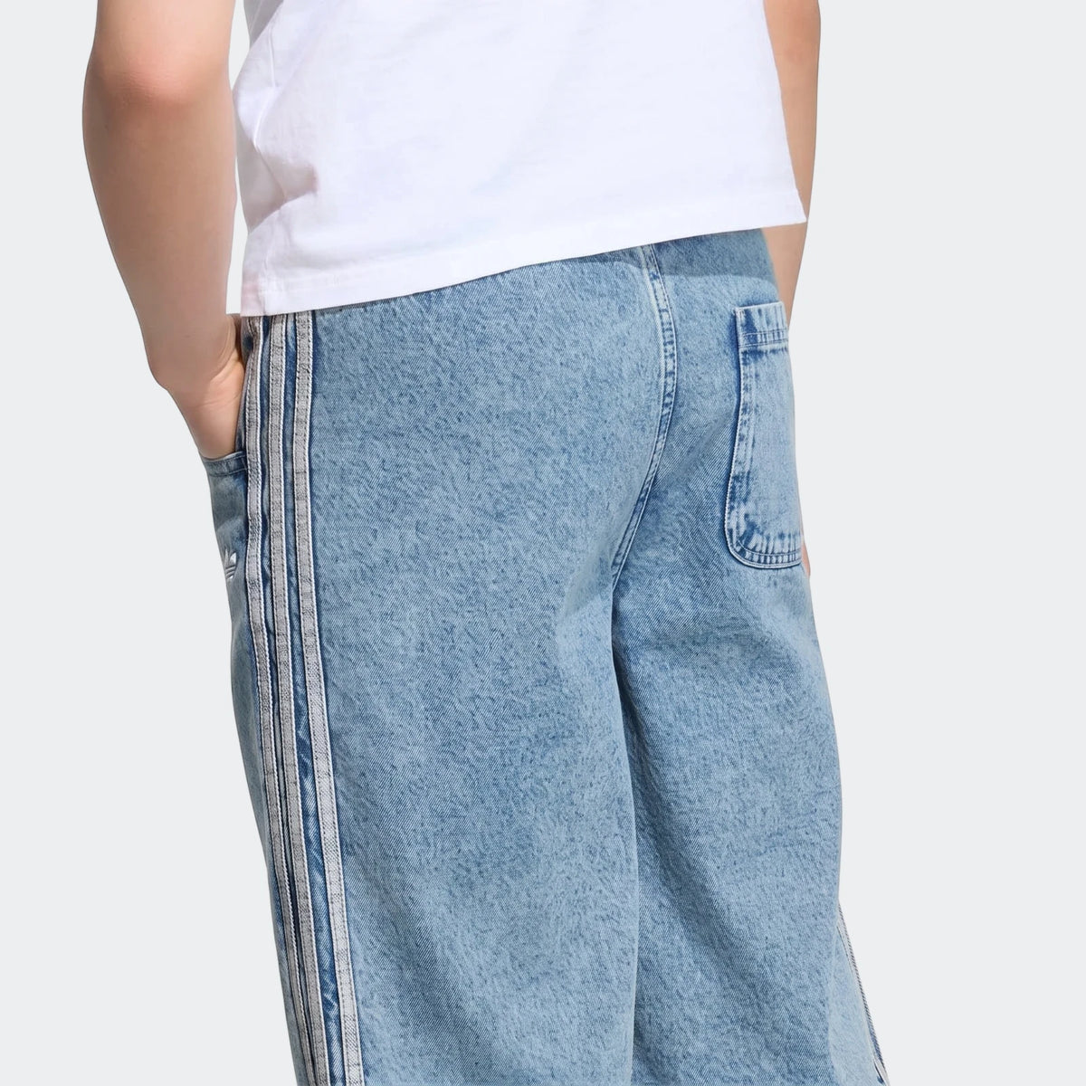 Person from waist up wearing light wash loose denim jorts with triple stripes and a white t-shirt, hands in pockets.