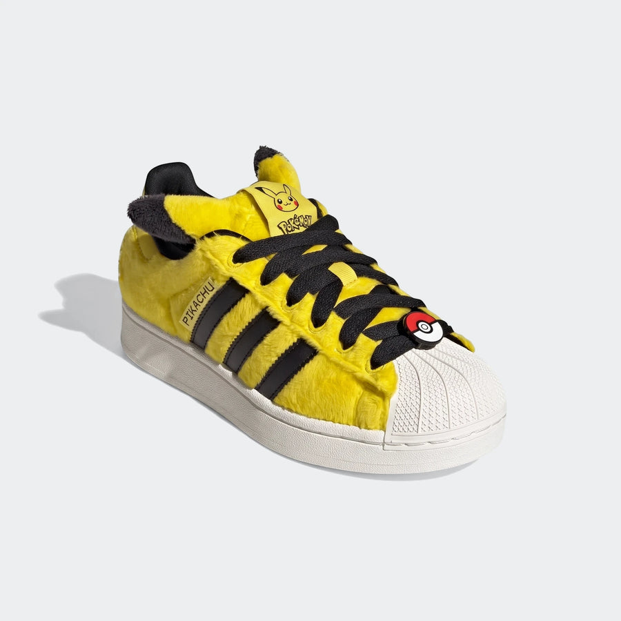 Yellow fuzzy Adidas Pokémon Superstar II shoes in a 3/4 view, featuring black stripes, Pikachu branding, and a Poké Ball