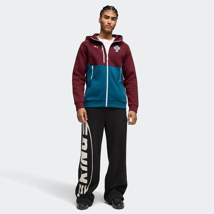 Full-body shot of a man wearing a maroon and teal Portugal Pumatech Full-Zip Hoodie and black sweatpants with a 'KINGS'