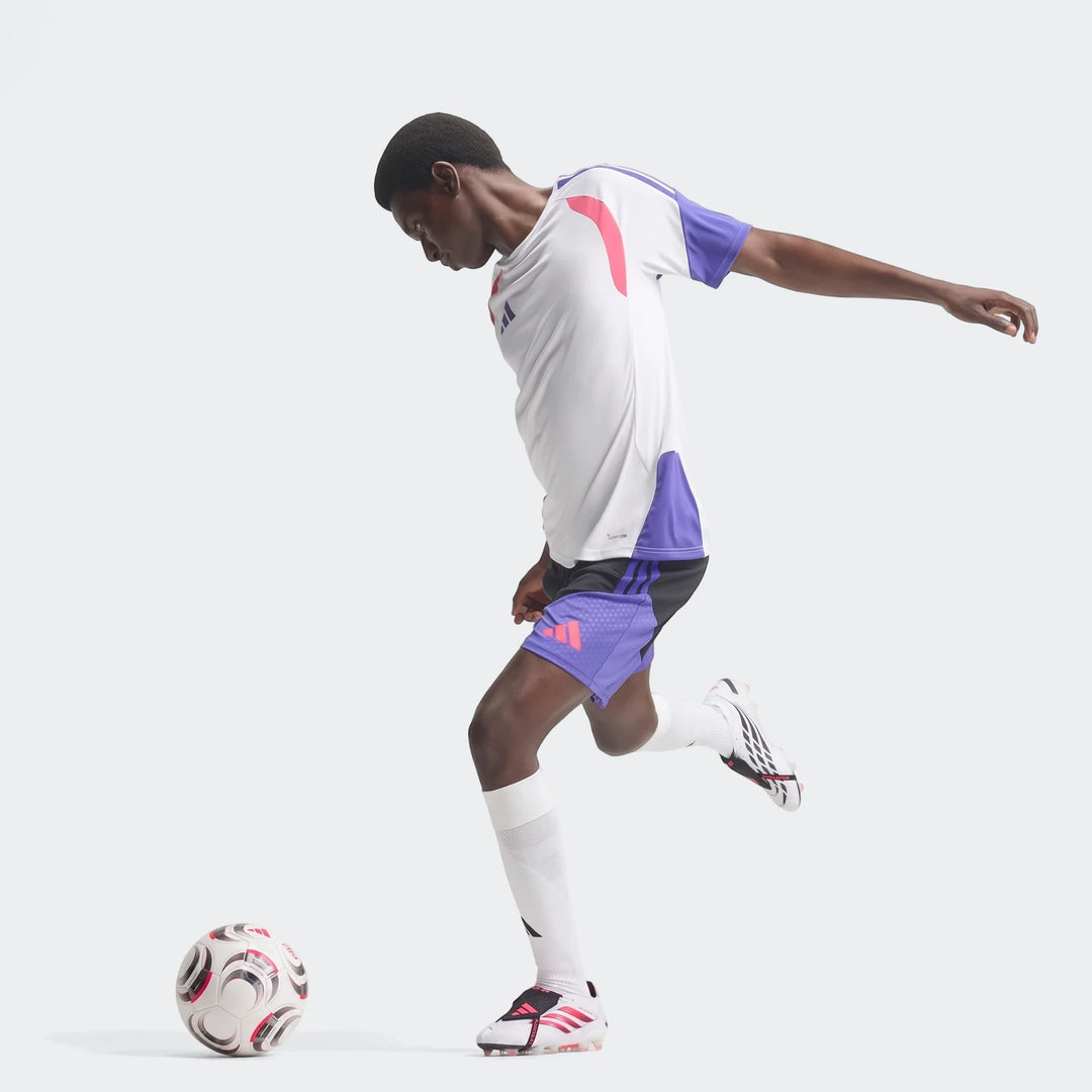 Male model wearing white and pink Predator Elite Fold-Over Tongue Firm Ground Football Boots, black and purple shorts, and a