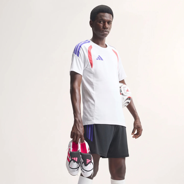 Man in white Adidas soccer jersey and black shorts holding Predator League Fold-Over Tongue Firm Ground Football Boots and a