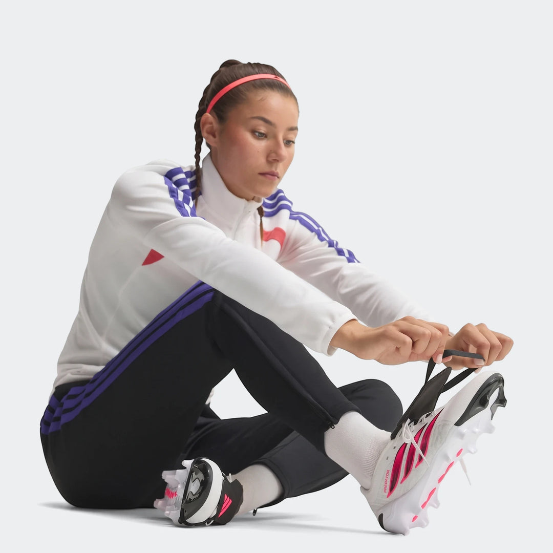 Female athlete lacing white and pink Predator League Fold-Over Tongue Firm Ground Football Boots on a clean studio floor.
