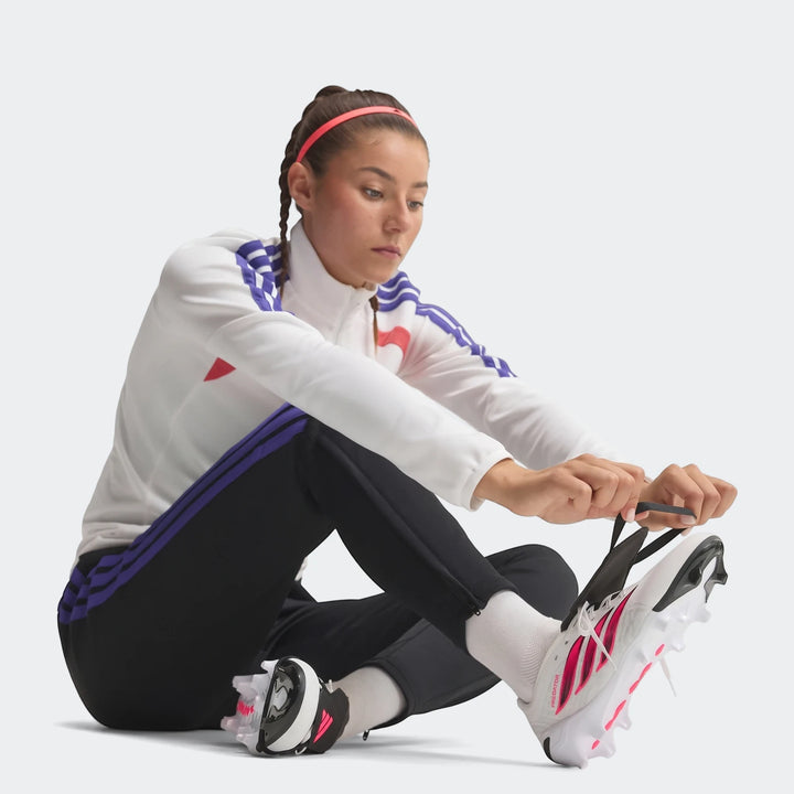 Female athlete lacing white and pink Predator League Fold-Over Tongue Firm Ground Football Boots on a clean studio floor.