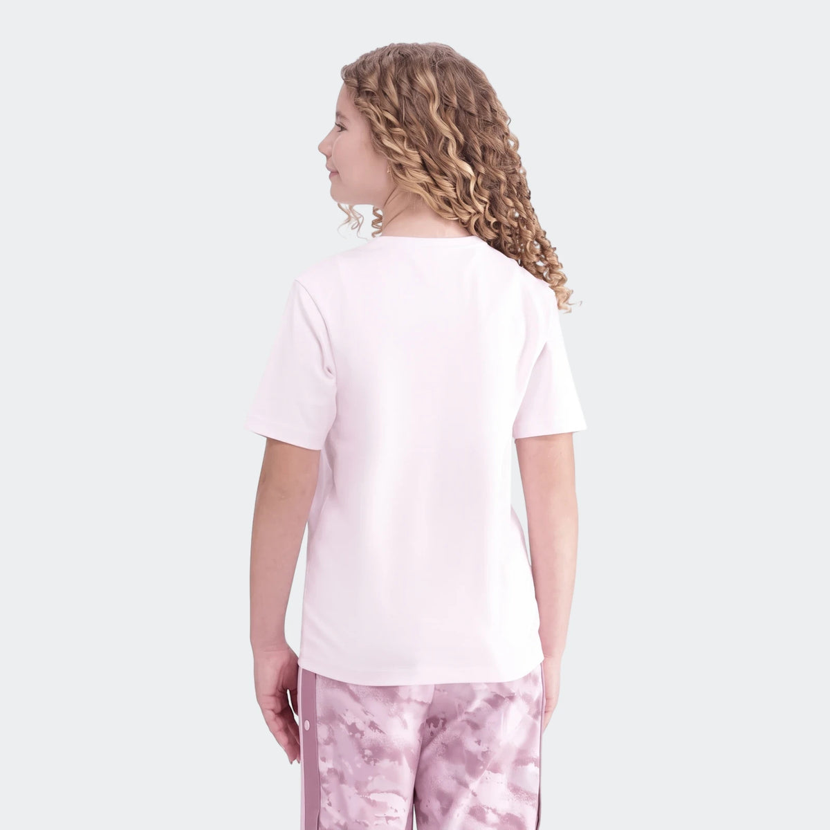 Young girl from behind wearing a pink Premium Essentials Tee and pink tie-dye shorts with curly hair.
