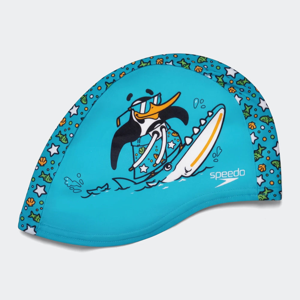 Printed blue polyester swim cap for kids featuring a fun cartoon graphic of a surfing penguin with sunglasses and the Speedo