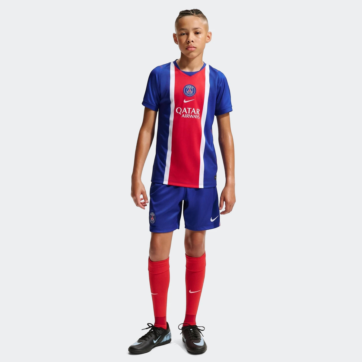 Young boy models the Paris Saint-Germain 2026/27 Stadium Home Nike Dri-Fit Soccer Replica Jersey, blue shorts, and red socks.