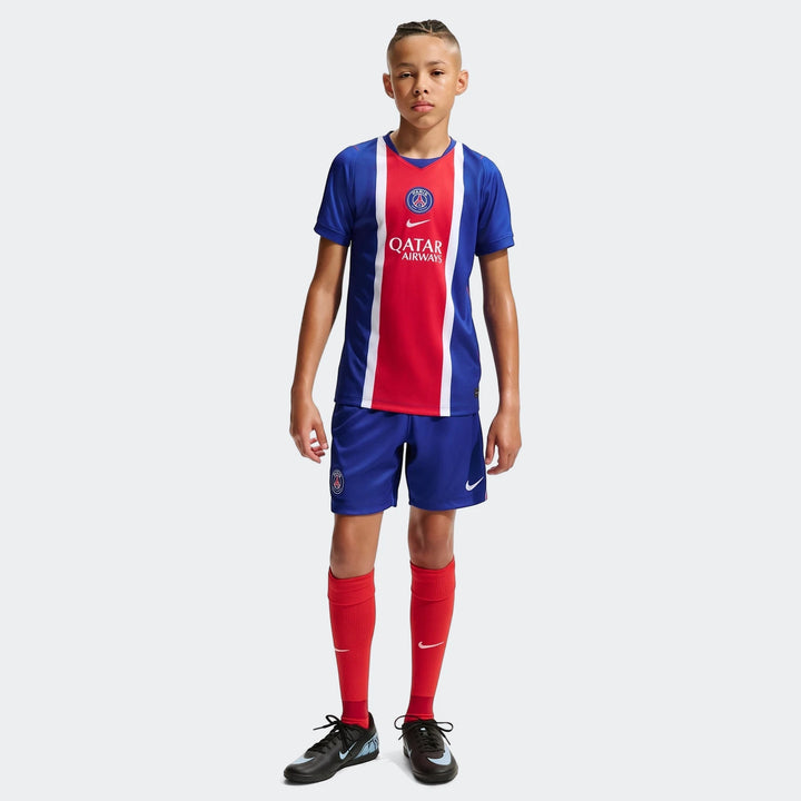 Young boy models the Paris Saint-Germain 2026/27 Stadium Home Nike Dri-Fit Soccer Replica Jersey, blue shorts, and red socks.