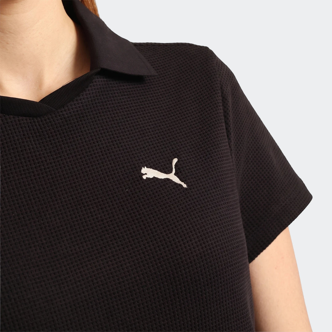 Close-up of a person wearing a black Puma Class Pinnacle Dress, showcasing its waffle knit texture and embroidered Puma logo.