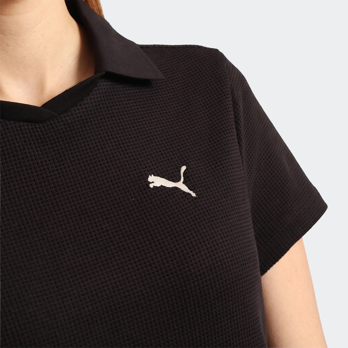 Close-up of a person wearing a black Puma Class Pinnacle Dress, showcasing its waffle knit texture and embroidered Puma logo.