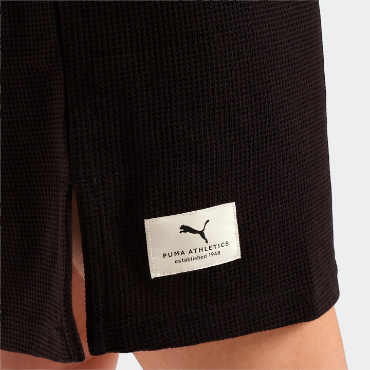 Close-up of a black Puma Class Pinnacle Dress made from waffle-knit fabric, showing the side split and Puma Athletics label