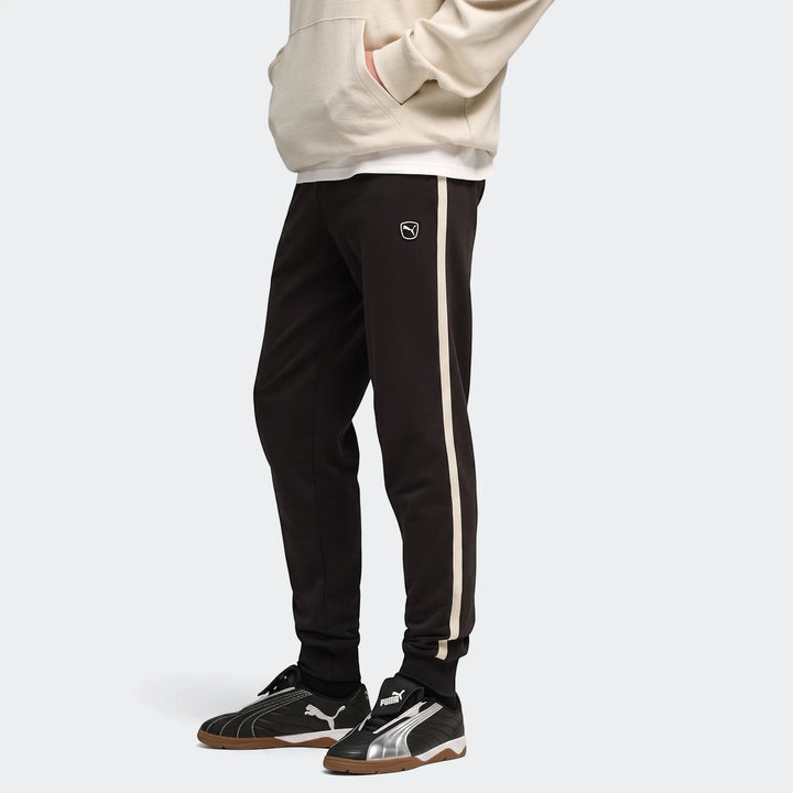 Black PUMA Ess Elevated sweatpants with a cream stripe, worn by a person from the waist down, paired with black and silver
