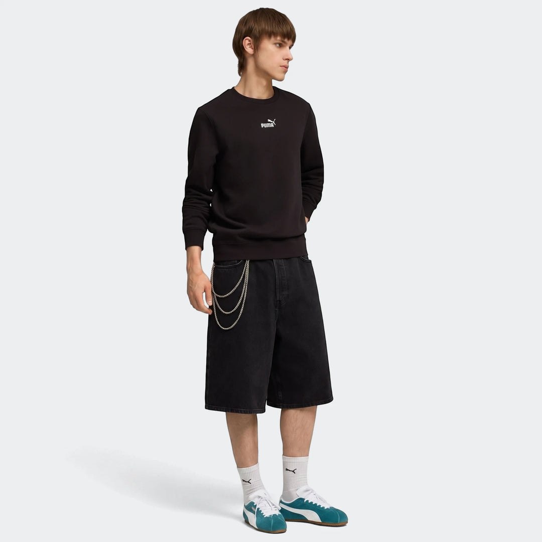 Male model in black Puma Ess No.1 Logo Crew sweatshirt, black shorts, and teal sneakers on a plain background.