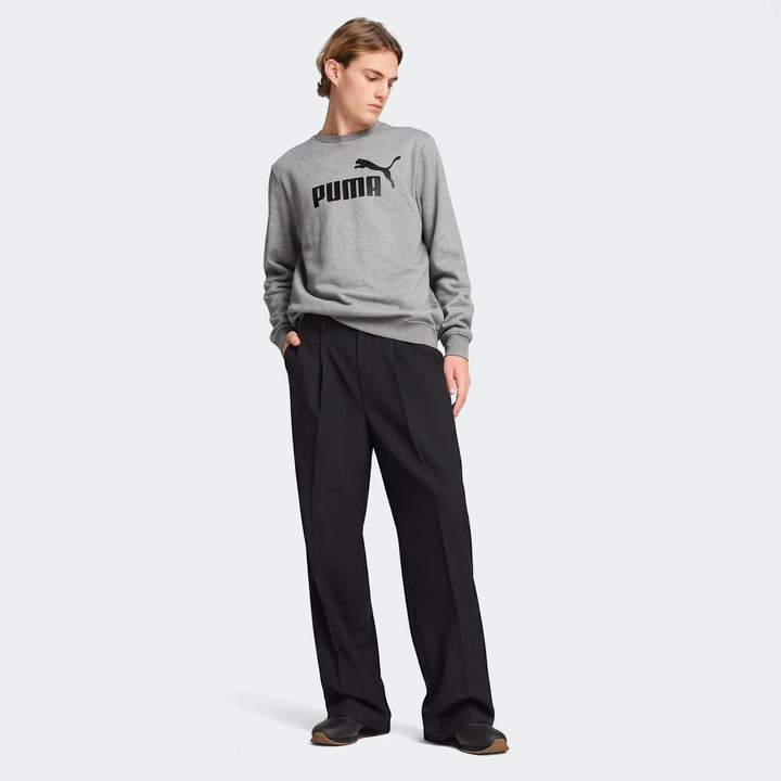 Full body shot of a male model wearing a grey Puma Ess No.1 Logo Crew sweatshirt and black pleated pants, with black shoes
