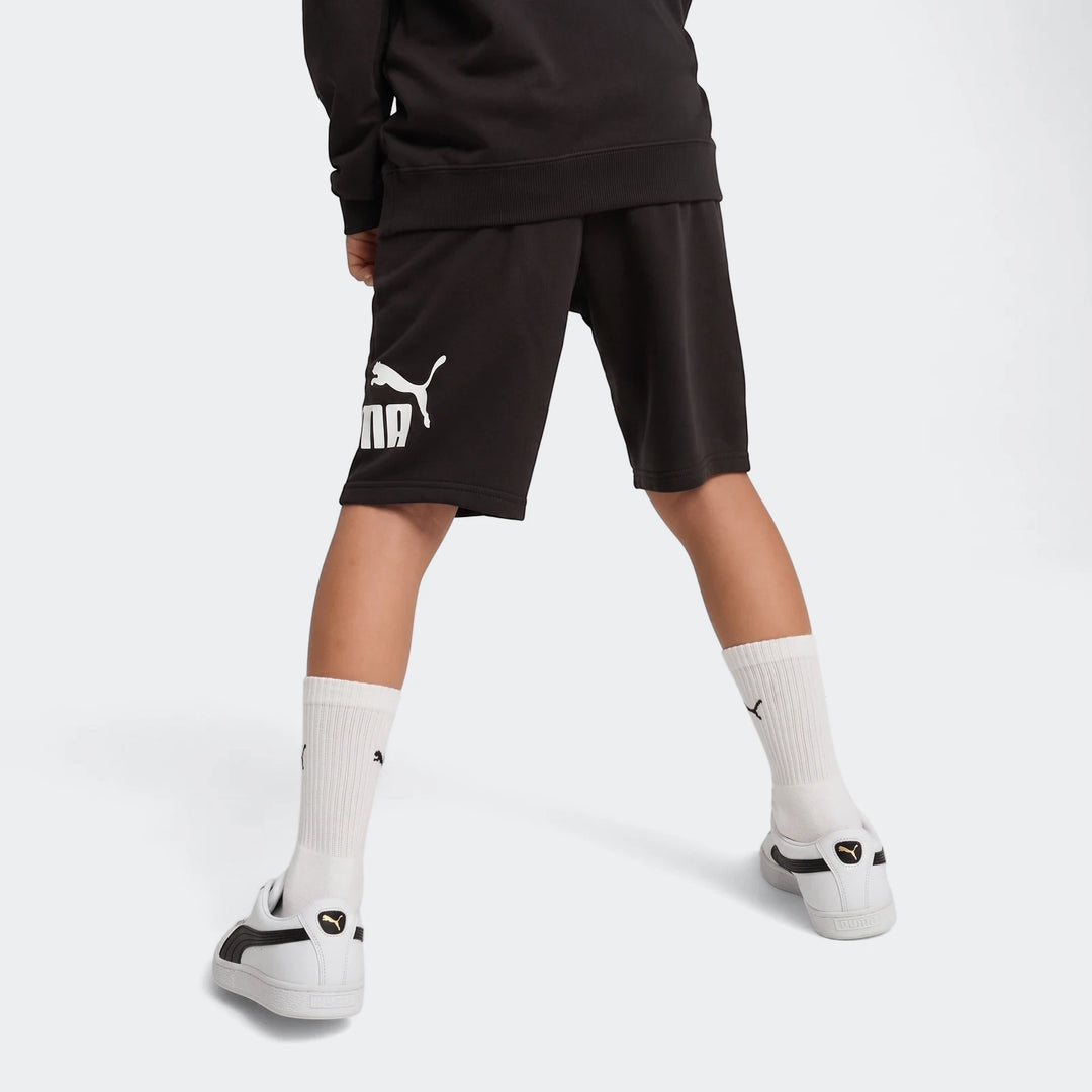 Black Puma Ess No. 1 Logo Shorts worn by a child, viewed from behind showing the legs and white sneakers.