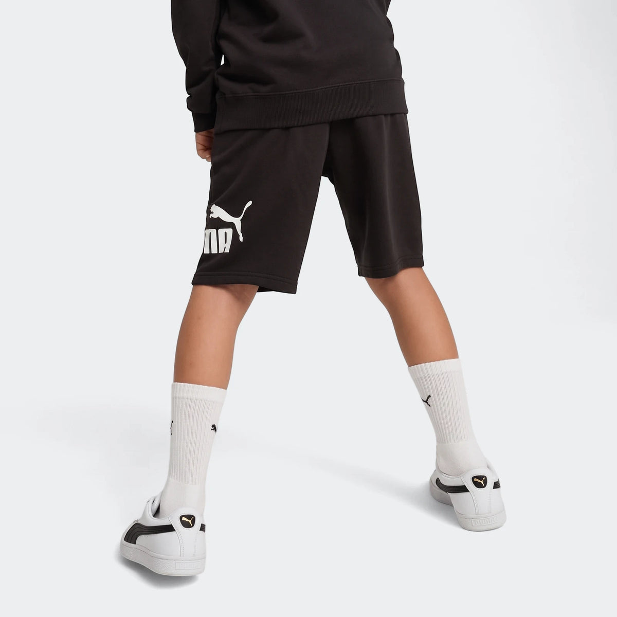 Black Puma Ess No. 1 Logo Shorts worn by a child, viewed from behind showing the legs and white sneakers.