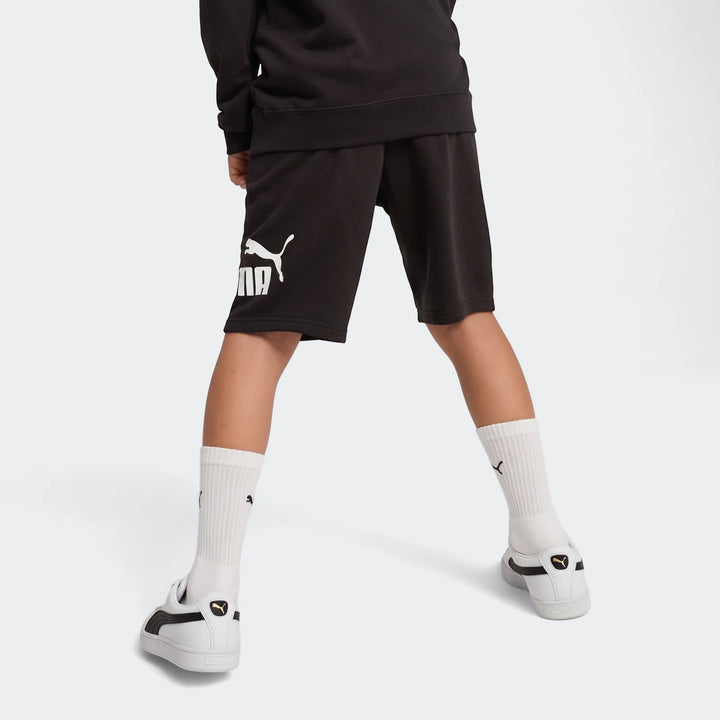 Black Puma Ess No. 1 Logo Shorts worn by a child, viewed from behind showing the legs and white sneakers.