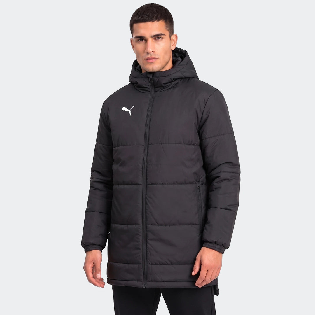 Front view of a male model wearing a black Puma Mens Bench Jacket. The quilted, hooded jacket features a full-zip closure