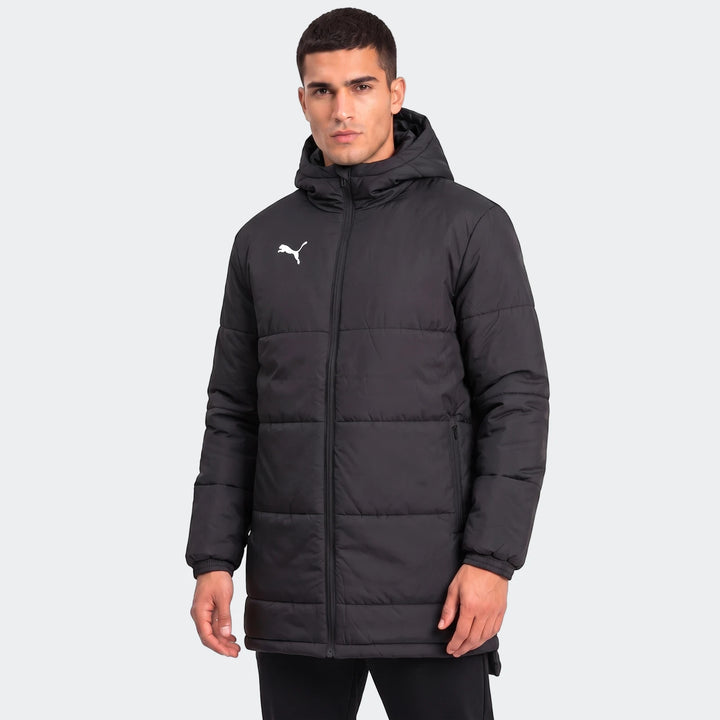 Front view of a male model wearing a black Puma Mens Bench Jacket. The quilted, hooded jacket features a full-zip closure