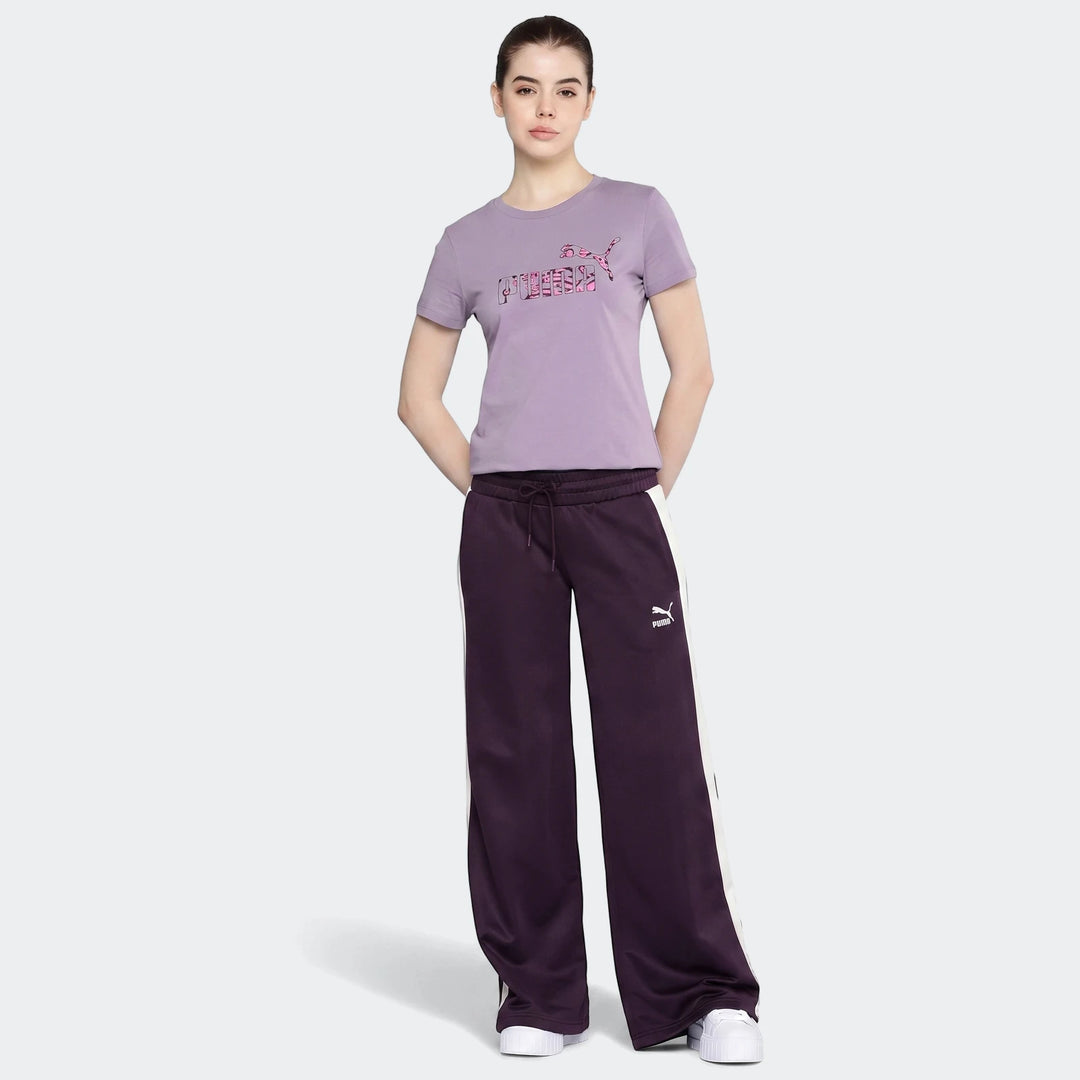 Woman wearing a purple Puma Power Hypernatural t-shirt and dark purple track pants with white stripes, standing on a grey