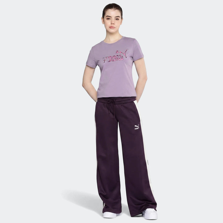 Woman wearing a purple Puma Power Hypernatural t-shirt and dark purple track pants with white stripes, standing on a grey