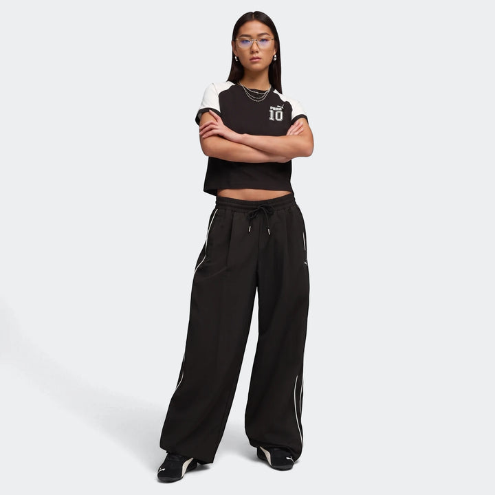 Woman wearing black PUMA Speedcat Wedge OG sneakers, black wide-leg pants, and a black and white crop top in a studio.