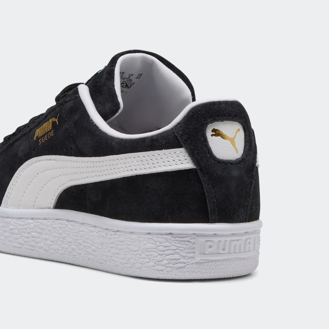 Black Puma Suede Classic Youth sneakers, showing the back-quarter view with white sole, side stripe, and gold logo.