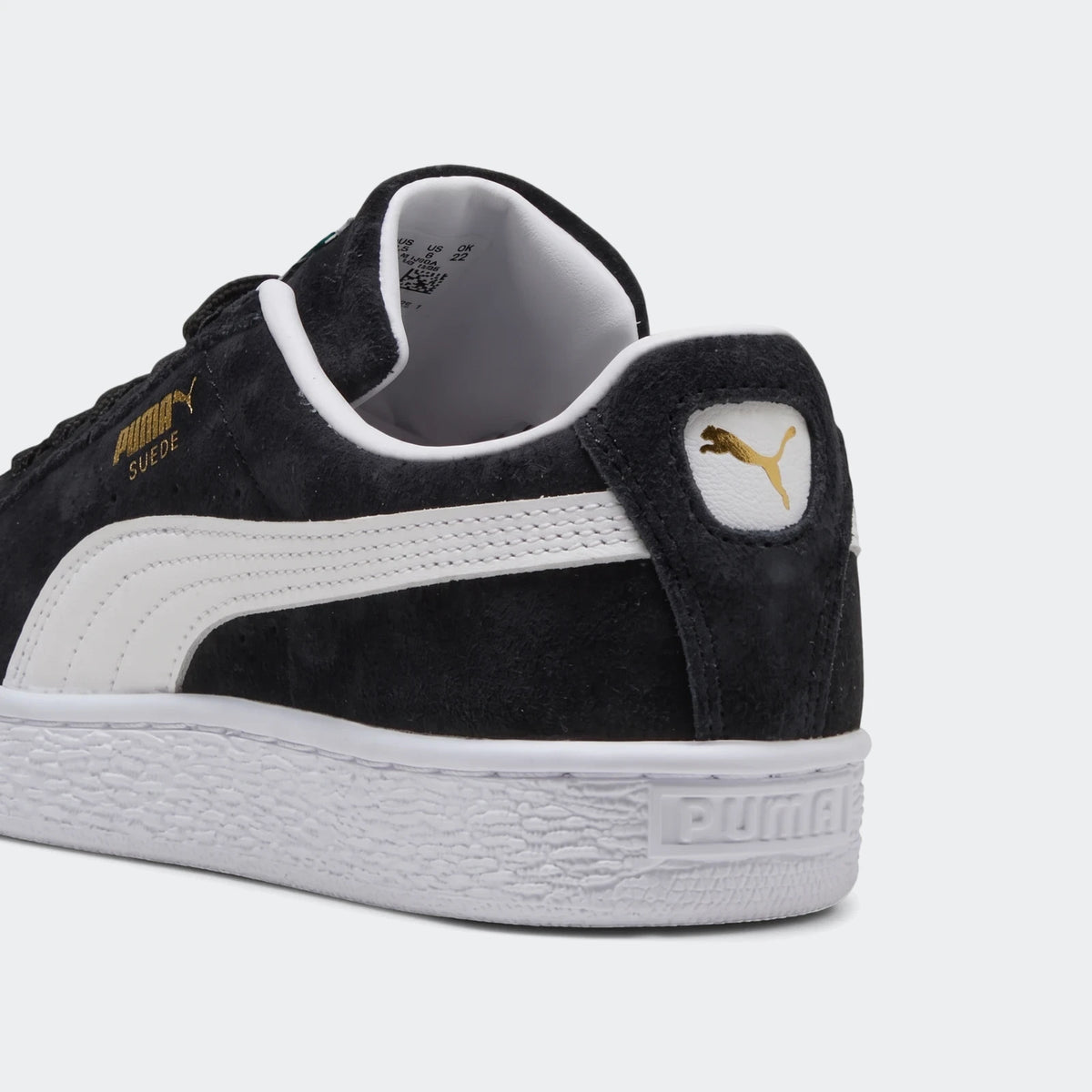 Black Puma Suede Classic Youth sneakers, showing the back-quarter view with white sole, side stripe, and gold logo.
