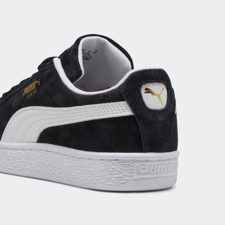 Black Puma Suede Classic Youth sneakers, showing the back-quarter view with white sole, side stripe, and gold logo.