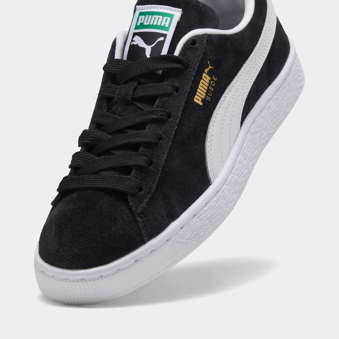 Black Puma Suede Classic Youth sneakers with white side stripe, black laces, and suede material, shown in a close-up studio
