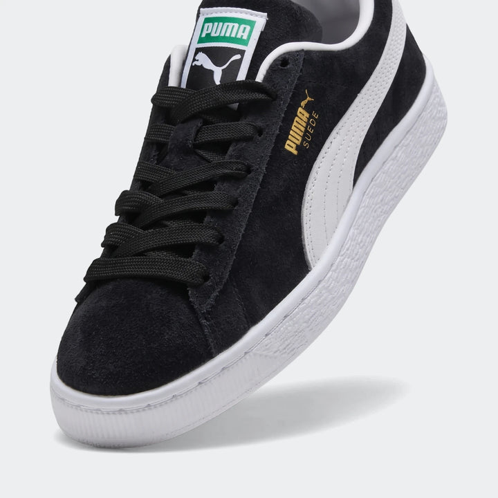 Black Puma Suede Classic Youth sneakers with white side stripe, black laces, and suede material, shown in a close-up studio