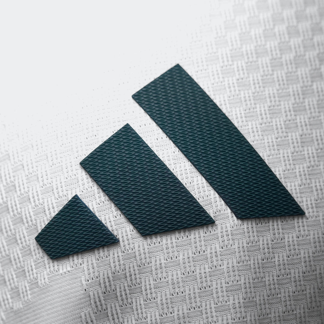 Close-up of a dark green Adidas logo with three stripes on the white textured fabric of the Real Madrid 25/26 Authentic Home