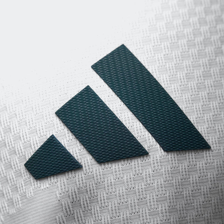 Close-up of a dark green Adidas logo with three stripes on the white textured fabric of the Real Madrid 25/26 Authentic Home