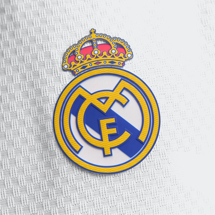 Close-up view of the Real Madrid 25/26 Authentic Home Jersey, showing the club's white, blue, red, and yellow logo patch.