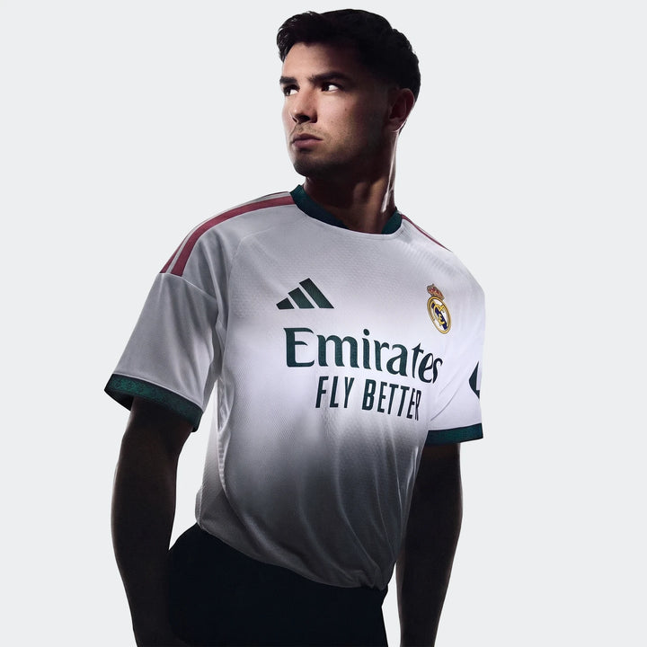 Real Madrid 25/26 Authentic Home Jersey worn by a male model, featuring the white jersey with green and red accents in a