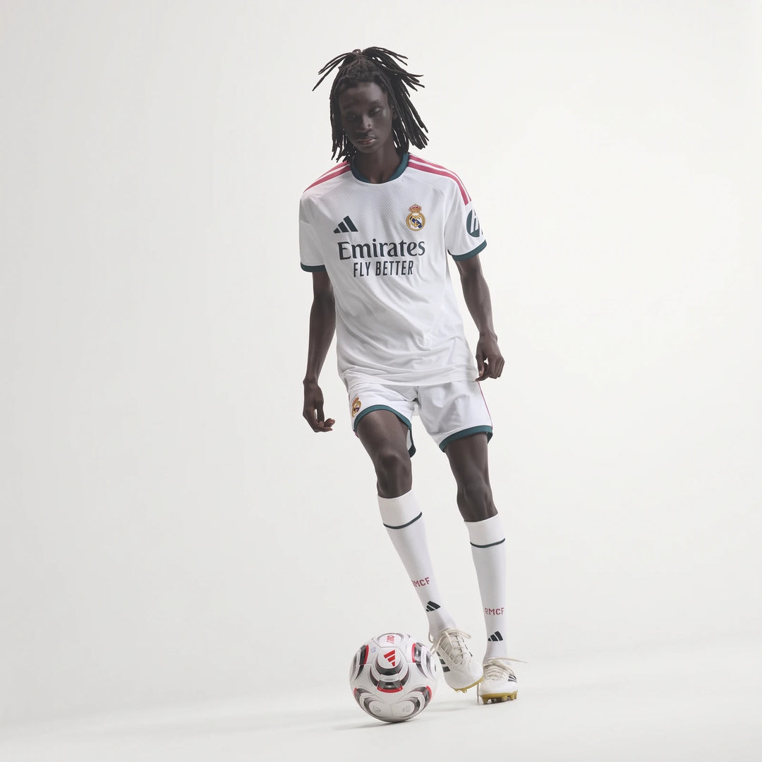 Real Madrid 25/26 Authentic Home Jersey in white with pink stripes and dark green trim, worn by a model playing soccer.