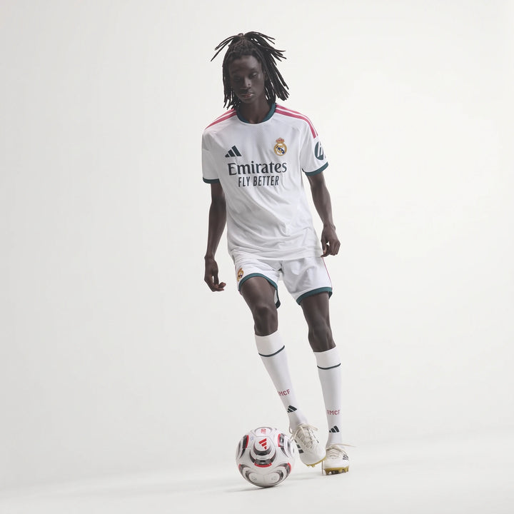 Real Madrid 25/26 Authentic Home Jersey in white with pink stripes and dark green trim, worn by a model playing soccer.