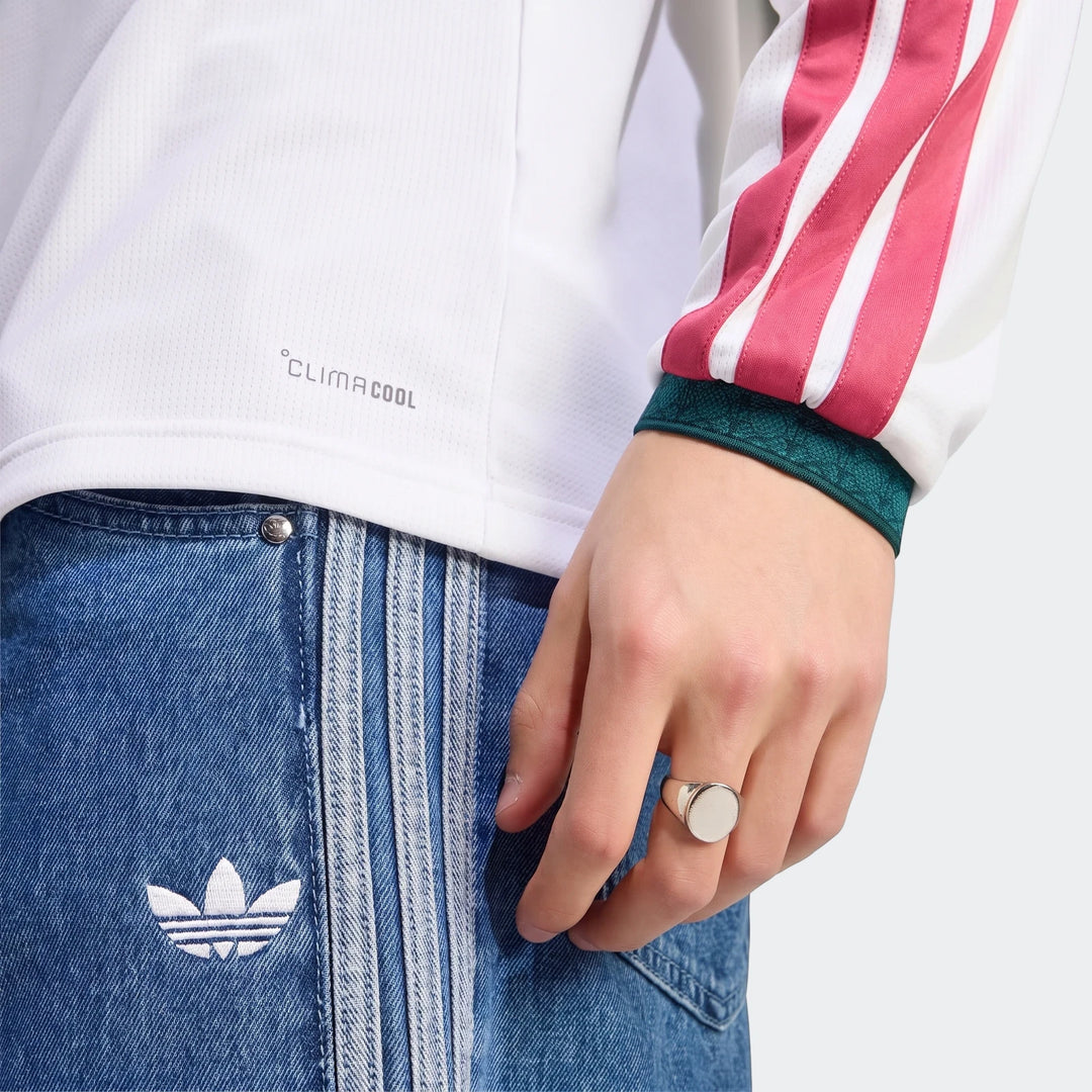 Close-up of a person wearing the white Real Madrid 25/26 Long Sleeve Home Jersey with pink stripes, paired with blue denim