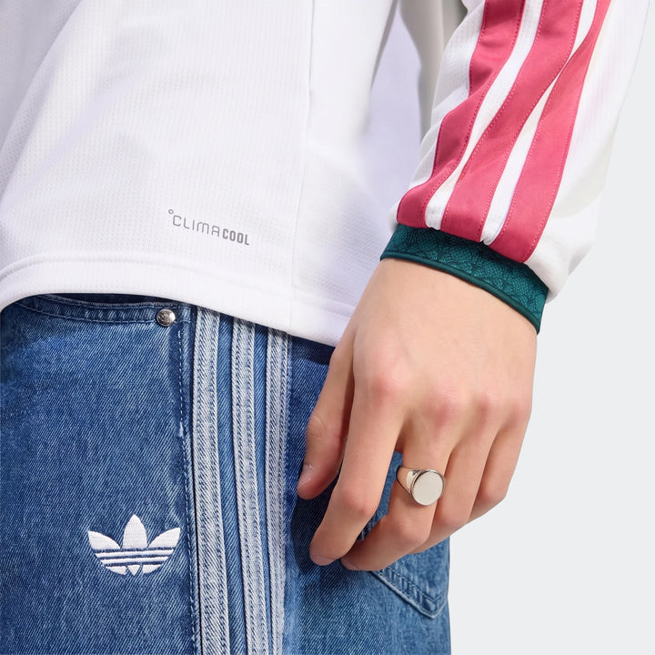 Close-up of a person wearing the white Real Madrid 25/26 Long Sleeve Home Jersey with pink stripes, paired with blue denim